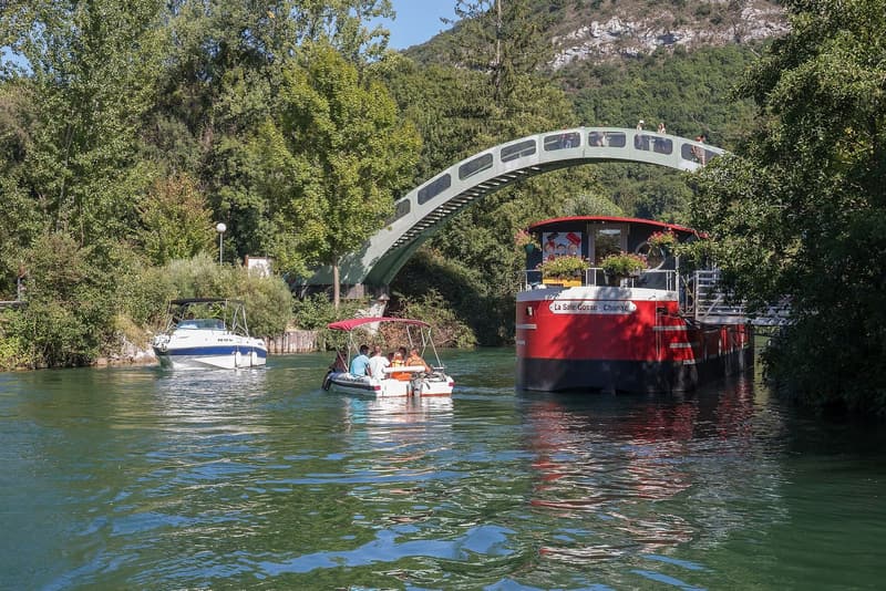 Une passerelle en arc au-dessus du canal de Savières, des bateaux amarrés