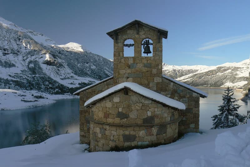 La chapelle de Roselend sous la neige, le lac et les sommets enneigés derrière